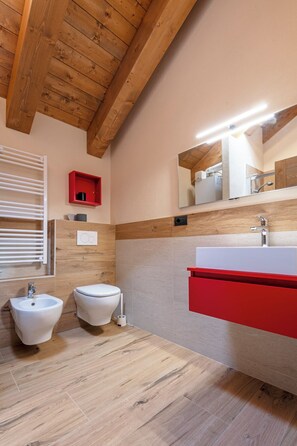 Ein modernes Badezimmer mit Holzbalken, einem roten Schrank, zwei Duschtoiletten und einem Spiegel.