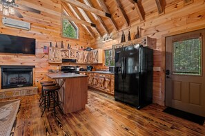 A wooden cabin interior with a kitchen, bar area, and a fireplace. - Pappy's Peace cozy cabin atop the Alabama Alps! (Mentone)