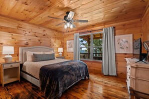 A wooden cabin bedroom with a bed, nightstands, a dresser, a ceiling fan, and a window with curtains. - Pappy's Peace cozy cabin atop the Alabama Alps! (Mentone)