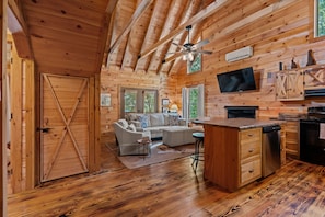 Ein Holzblockhaus-Innenraum mit Wohnbereich, Küche und Deckenventilator.