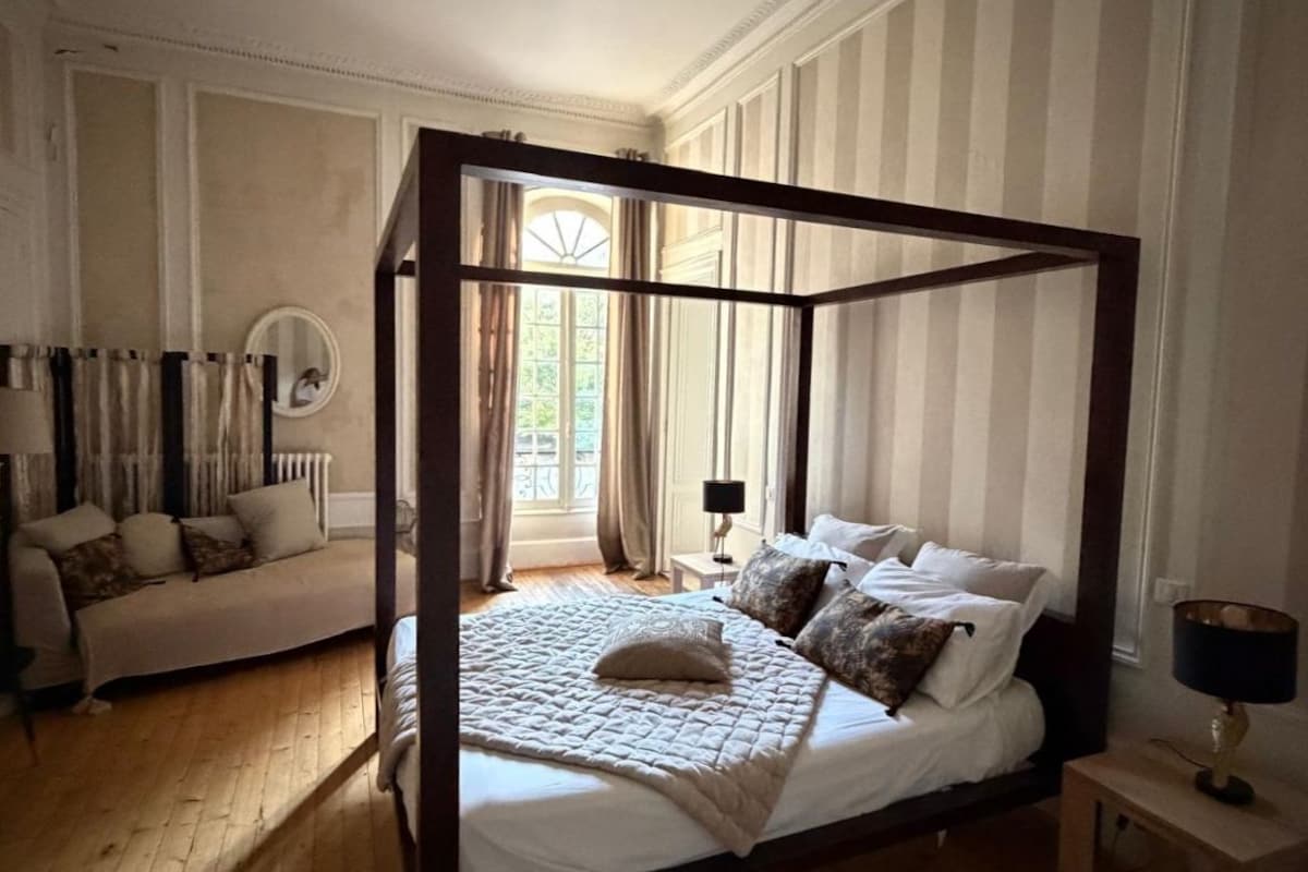 A four-poster bed with a quilt, a bedside table with a lamp, and a sofa with cushions.