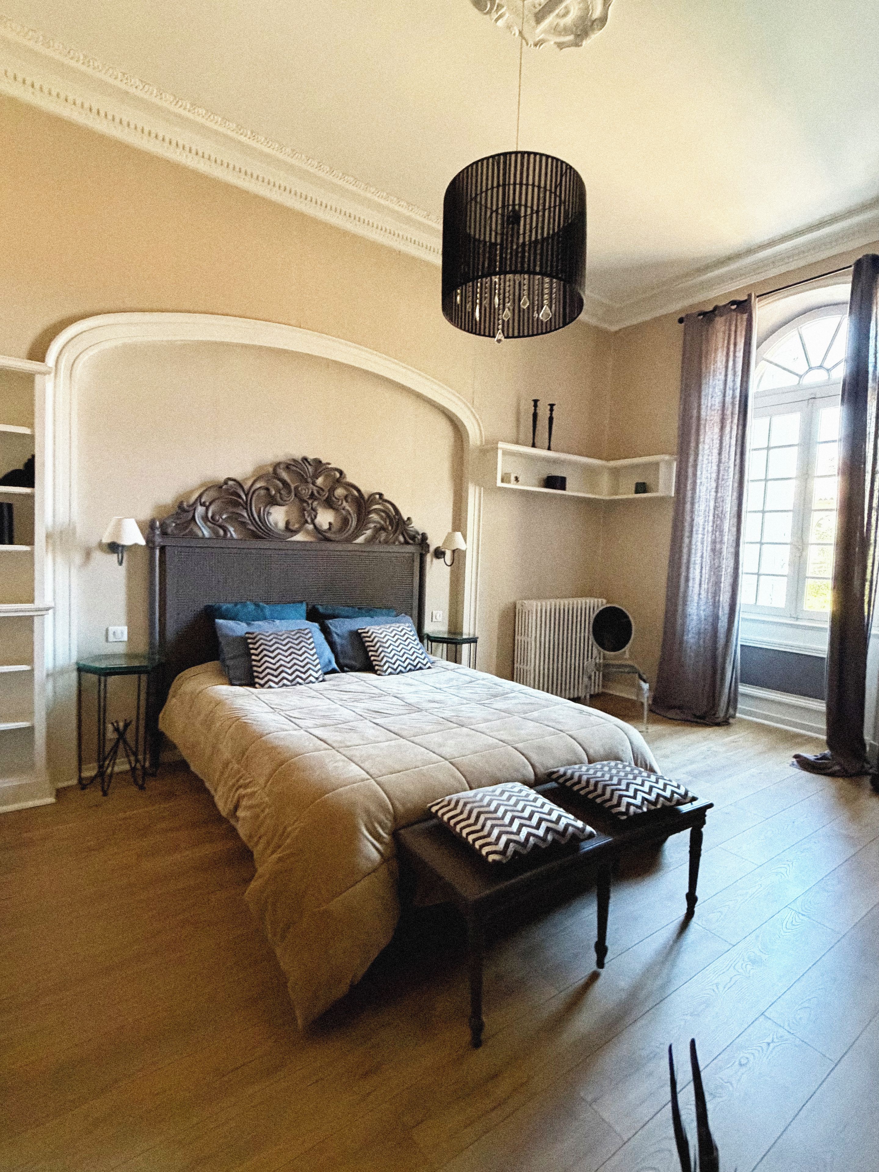 Een slaapkamer met een groot bed, een nachtkastje, een lamp en een raam met gordijnen.