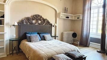 Een slaapkamer met een groot bed, een nachtkastje, een lamp en een raam met gordijnen.