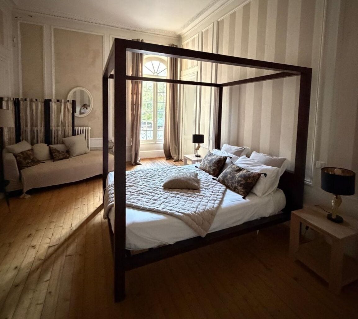 Un lit à baldaquin avec une courtepointe, une table de chevet avec une lampe et un canapé avec des coussins.