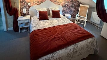 A bedroom with a bed, nightstands, a chair, and a wall with floral wallpaper.