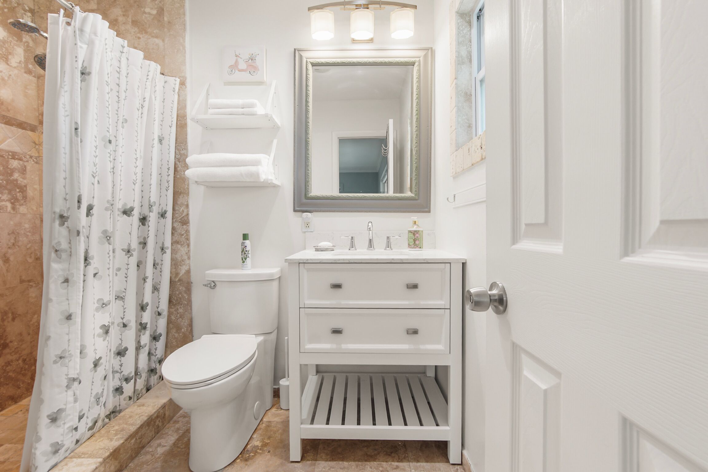 Ein Badezimmer mit Toilette, einem Waschbecken mit Spiegel darüber und einer Duschkabine mit Blumenmuster.