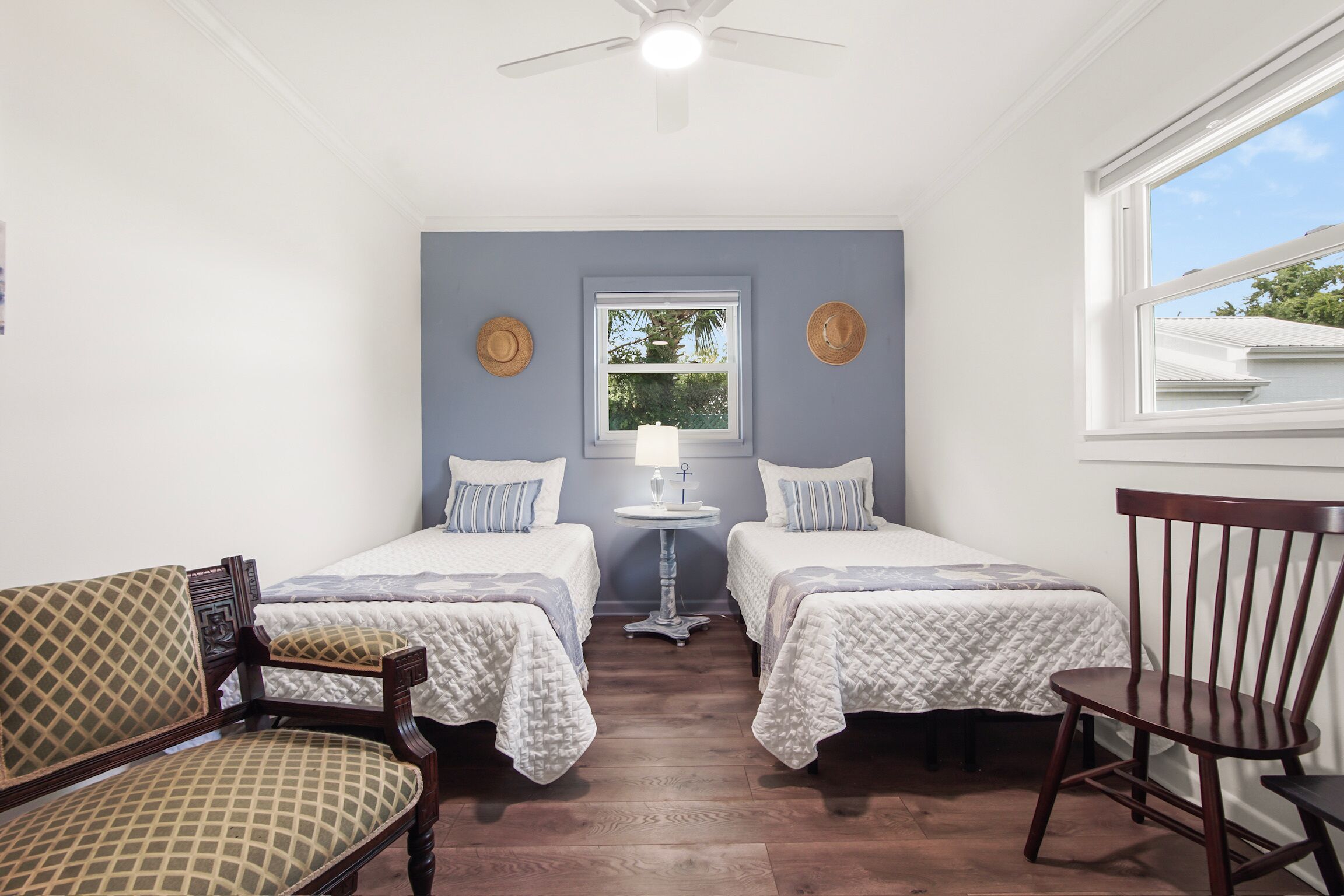 Une chambre avec deux lits, une chaise, une petite table et un ventilateur de plafond.