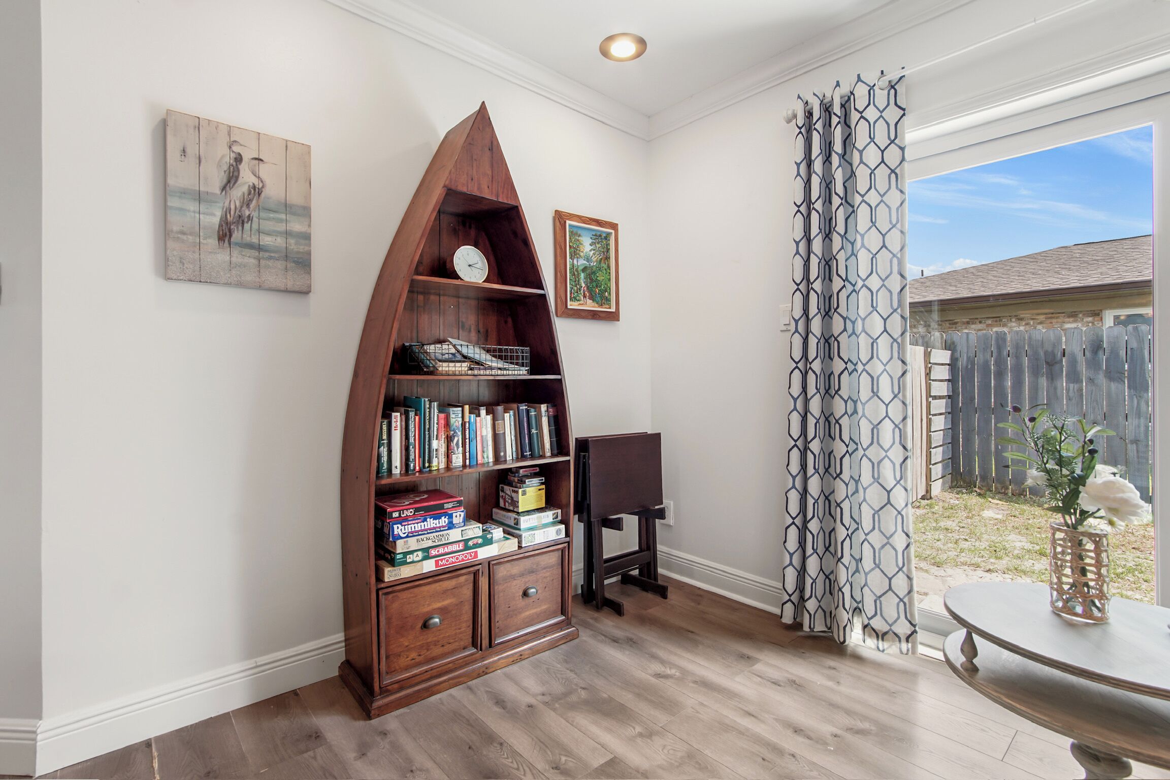 A room with a wooden bookshelf, a clock, and a framed picture on the wall.