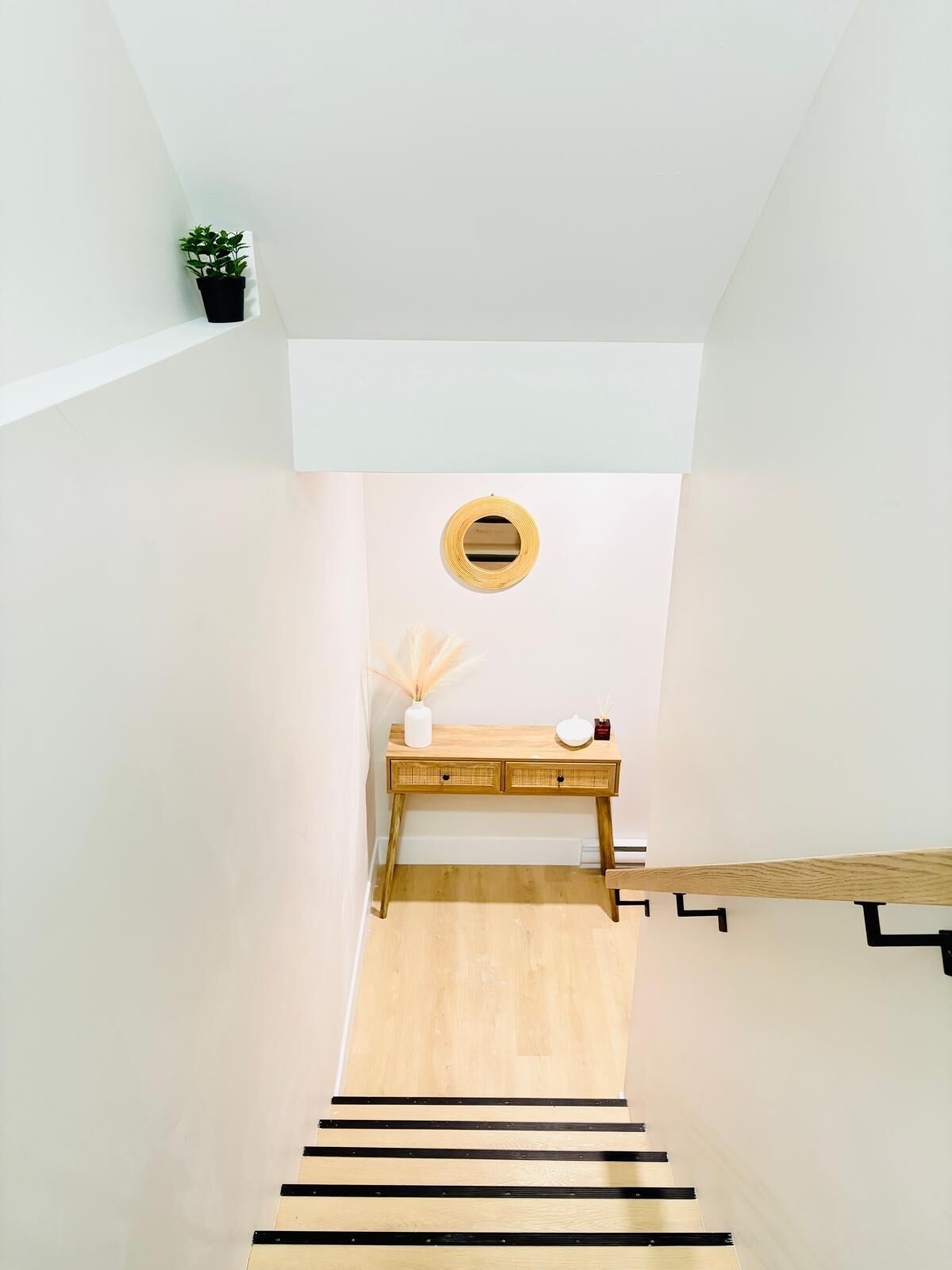 Una escalera con acabado de madera, una pequeña mesa con un florero y una vela, y una planta en maceta en el rellano.