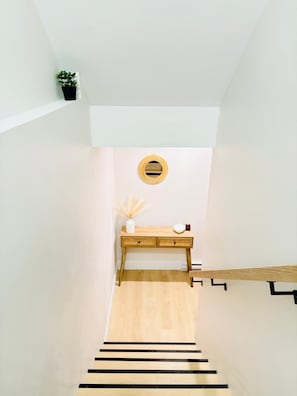 Eine Treppe mit Holzvertäfelung, ein kleiner Tisch mit einer Vase und einer Kerze sowie eine Topfpflanze auf der Zwischenebene.