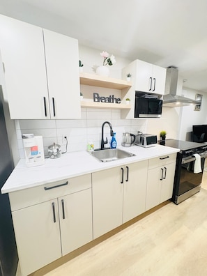 A modern kitchen with white cabinets, a stainless steel sink, a microwave, and a stove. - Modern Moncton home (Moncton)