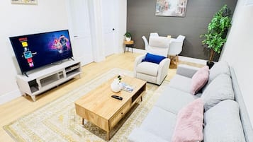 Ein modernes Wohnzimmer mit Flachbildfernseher, Couchtisch, grauem Sofa und weißem Sessel.