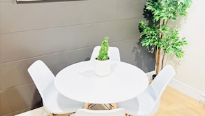 Habitació moderna amb una taula rodona blanca, quatre cadires blanques, una planta en test i un quadre a la paret.