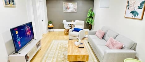 A modern living room with a flat-screen TV, a grey sofa, a coffee table, and a patterned rug.