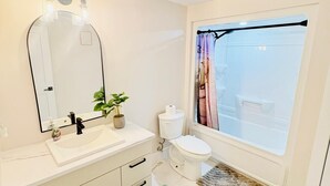 Un bany amb un rentapans, mirall, vàter i una finestra amb cortines.