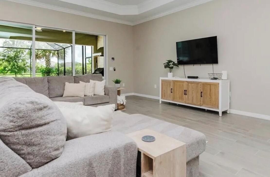 Una sala de estar con un sofá gris, un mueble de madera y un televisor en la pared.