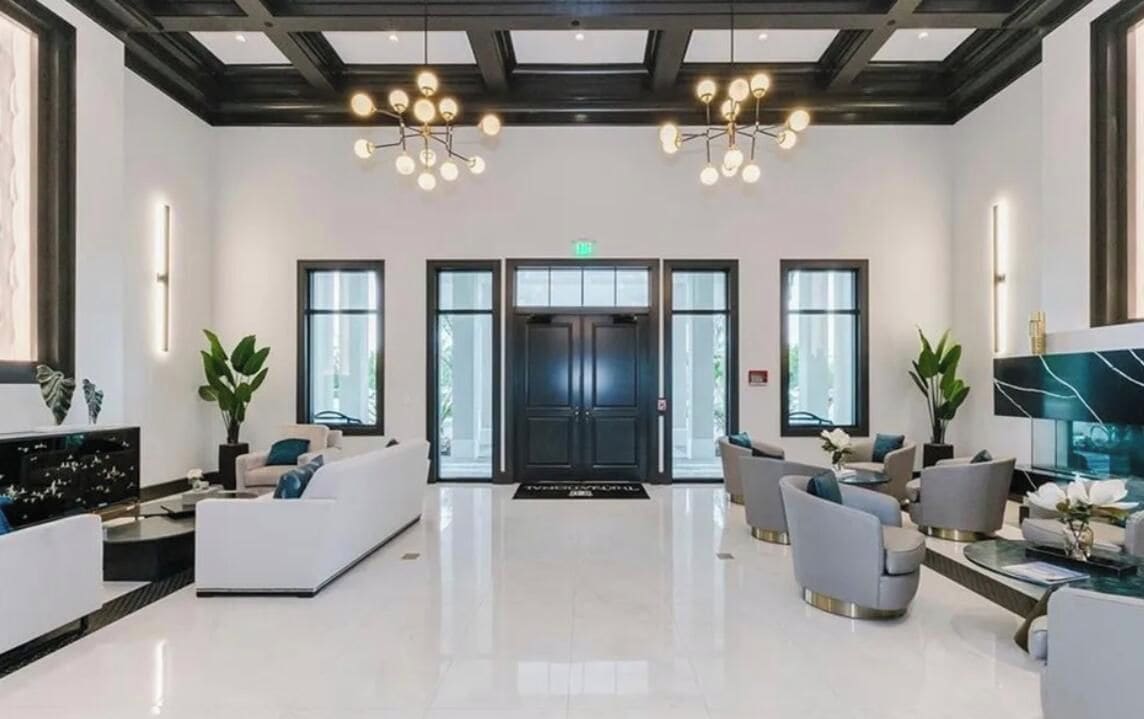 A spacious lobby with a modern chandelier, seating area, and a large television screen.