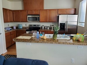 A kitchen with wooden cabinets, a microwave, stove, refrigerator, granite countertop, and various kitchen items.