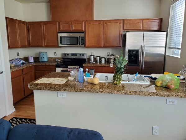 A kitchen with wooden cabinets, a microwave, stove, refrigerator, granite countertop, and various kitchen items.