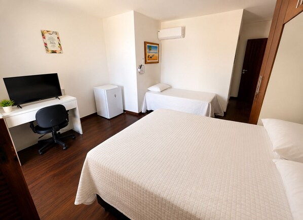 Une chambre d’hôtel comprenant un lit, un bureau avec un ordinateur, un petit réfrigérateur et une table de chevet.