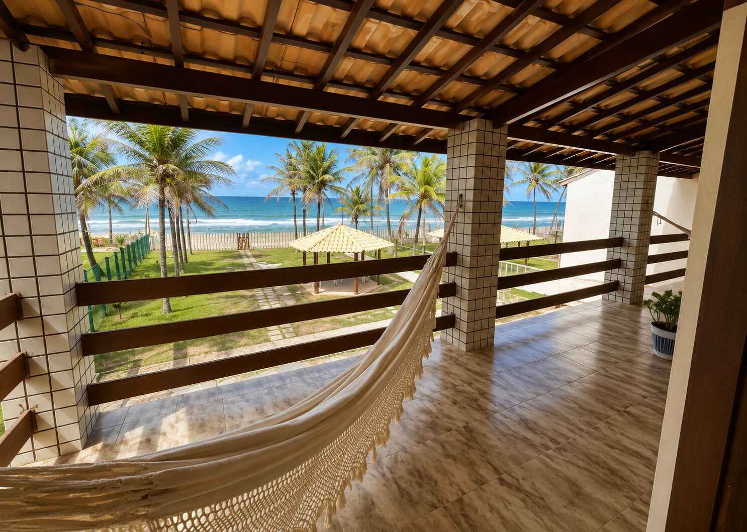 A hammock under a wooden ceiling with a view of the beach and palm trees.
