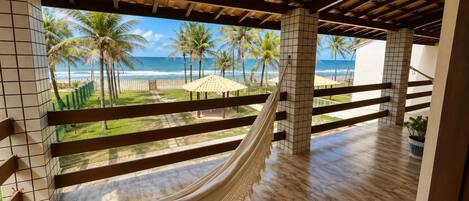 A hammock under a wooden ceiling with a view of the beach and palm trees.