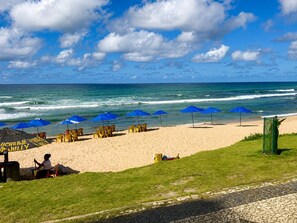 Una spiaggia con ombrelloni e sedie, una zona verde e vista sull'oceano.