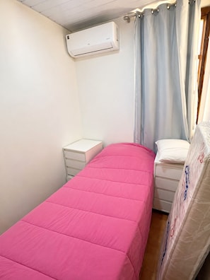 Una camera da letto con un letto singolo, un comodino, un'unità di condizionamento e una finestra con tende.