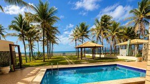 Piscina com deck azulejado, cercada por palmeiras e céu claro.