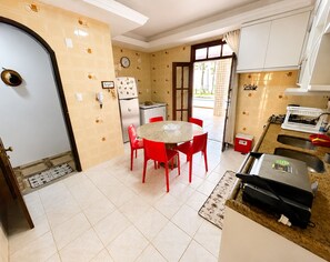 Une cuisine de taille réduite avec une table ronde, des chaises rouges, un réfrigérateur et une fenêtre avec des rideaux.