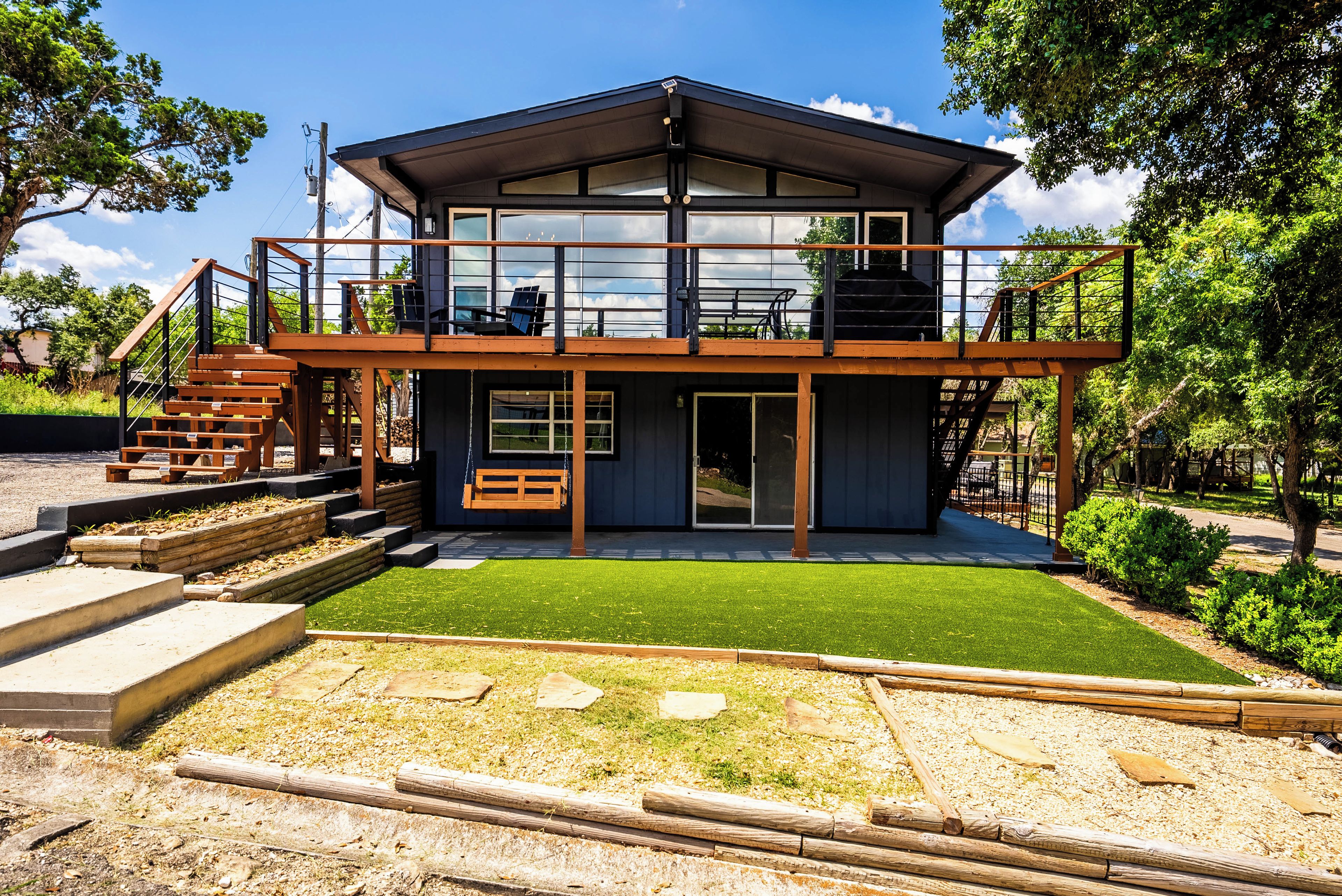Un bâtiment à deux étages doté d’un balcon, d’une balançoire et d’un espace patio avec une pelouse artificielle.