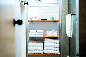 A bathroom with a towel rack, shelves with folded towels, and a shower area. - Canyon Lake Chalet - Firepit, Hot tub, Boat Parking (Canyon Lake)