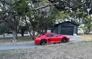 A red sports car parked in front of a garage with a tree-lined driveway. - Canyon Lake Chalet - Firepit, Hot tub, Boat Parking (Canyon Lake)