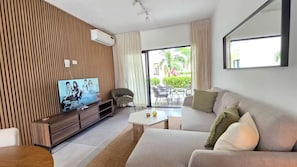 A modern living room with a flat-screen TV, sofa, coffee table, and a view of the outdoors through a glass door. - A magnificent oasis of peace just a few minutes from Bavaro Beach (Punta Cana)