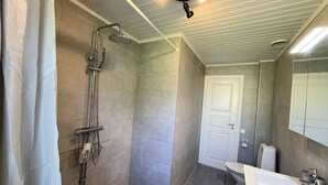 Et badeværelse med bruser, toilet, håndvask og spejl.