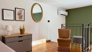 A room with a wooden floor, a grey dresser, a mirror, a framed artwork, an air conditioning unit, and a staircase with a metal railing. - Abbadia Quattro - Vintage Loft at the Mercato del Capo (Palermo)