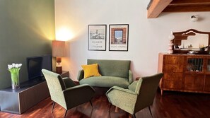 A living room with a sofa, two armchairs, a TV, a lamp, and a cabinet. There are two framed pictures on the wall. - Abbadia Quattro - Vintage Loft at the Mercato del Capo (Palermo)