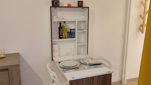 Una zona de menjador amb una taula preparada per a dues persones, un armari de fusta amb prestatges i una cadira blanca.