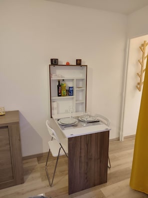 Ein Essbereich mit einem Tisch für zwei Personen, einem Holzschrank mit Regalen und einem weißen Stuhl.