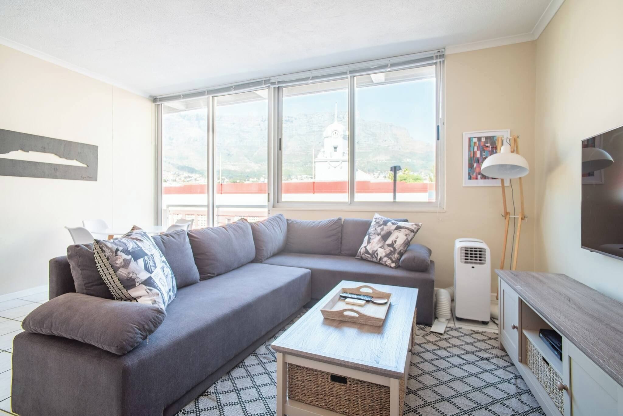 A modern living room with a grey sectional sofa, a coffee table, a TV stand, and a large window offering a city view.