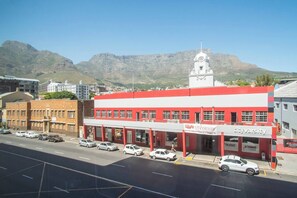 A red and white building with a clock tower, located in a city with mountains in the background. - 1-bedroom apartment in center of Cape Town (Cape Town)
