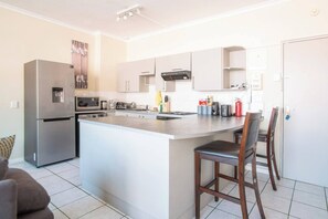 A modern kitchen with a central island, stainless steel appliances, and a dining area with a chair. - 1-bedroom apartment in center of Cape Town (Cape Town)