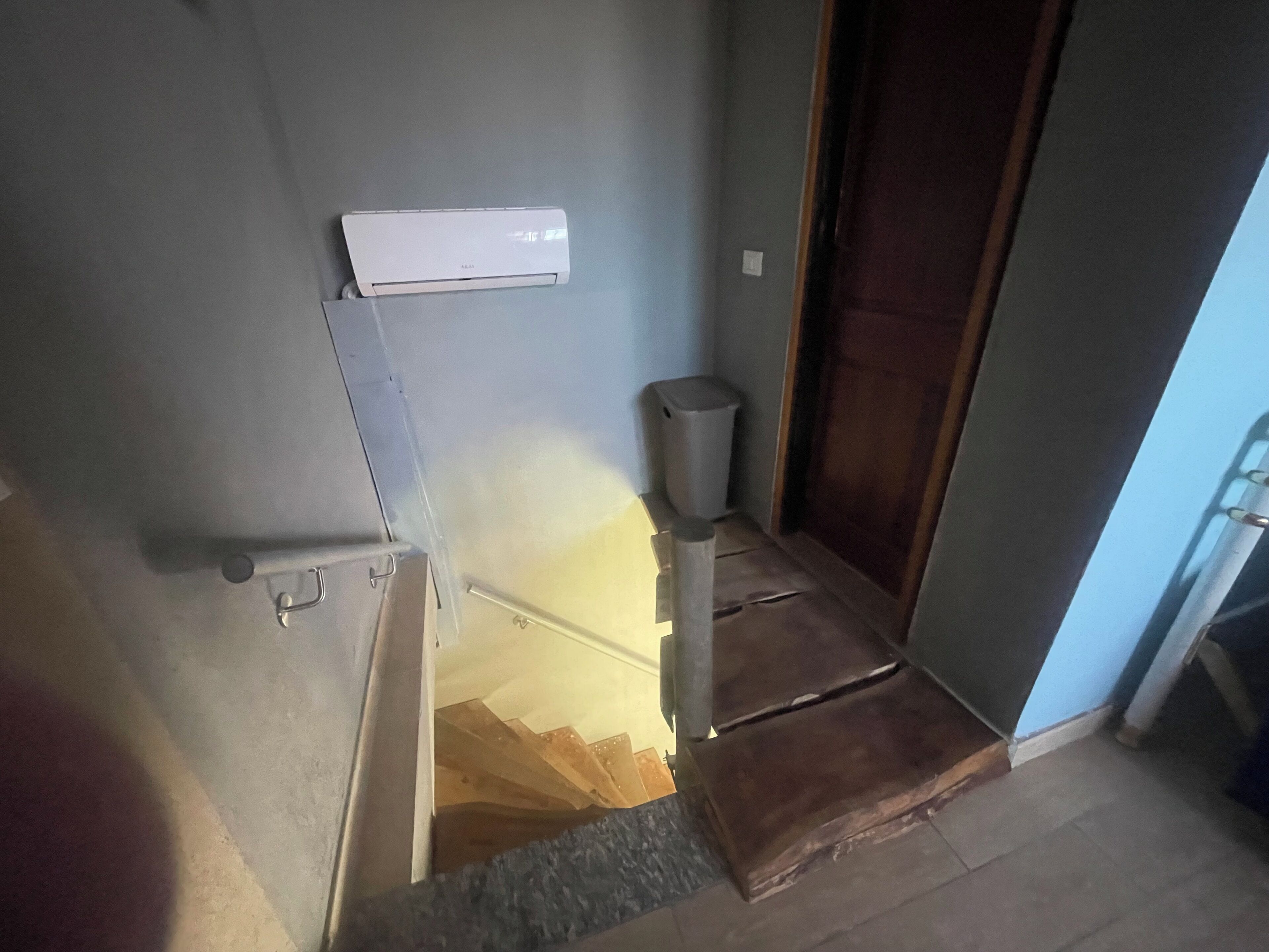 Un escalier étroit, avec une poubelle et un climatiseur fixé au mur.