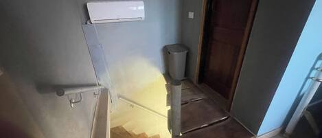 A narrow stairway with a trash bin and a wall-mounted air conditioning unit.