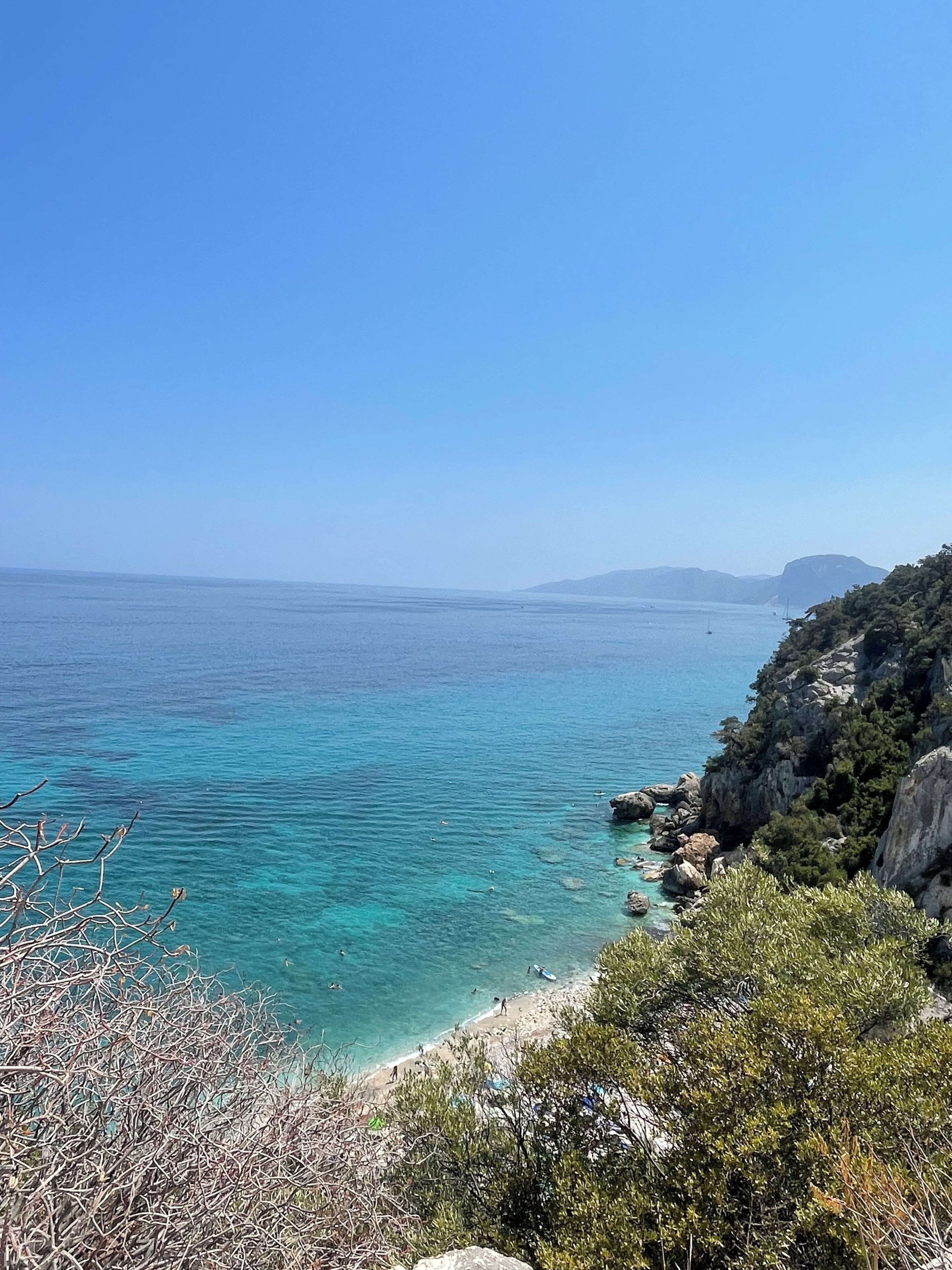 A coastal landscape with clear blue waters, rocky terrain, and sparse vegetation.