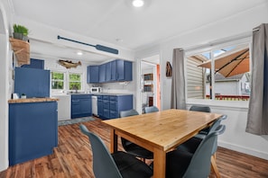 A compact kitchen with blue cabinets, a wooden dining table with chairs, and a view of the outdoors through a window.
