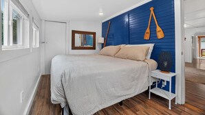Quarto com cama, mesa de cabeceira, abajur e parede azul com dois remo de madeira.