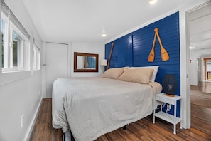 A bedroom with a bed, a nightstand, a lamp, and a blue wall with two wooden paddles.