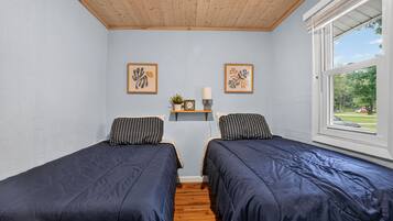 A bedroom with two beds, a shelf with decorative items, and a window with a view.