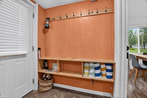 A room with a wooden shelf, a wall-mounted hookboard, a basket, and a door with blinds.